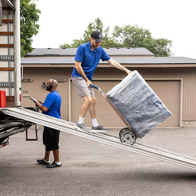 Professional long-distance movers unloading wrapped furniture out of moving truck